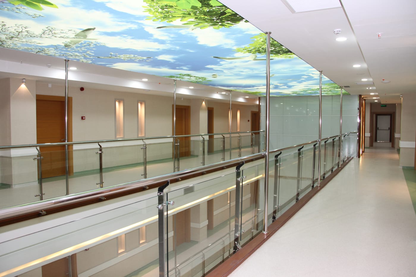 A bright, glass-railed patient corridor inside a facility operating under the Erbil International Hospital brand